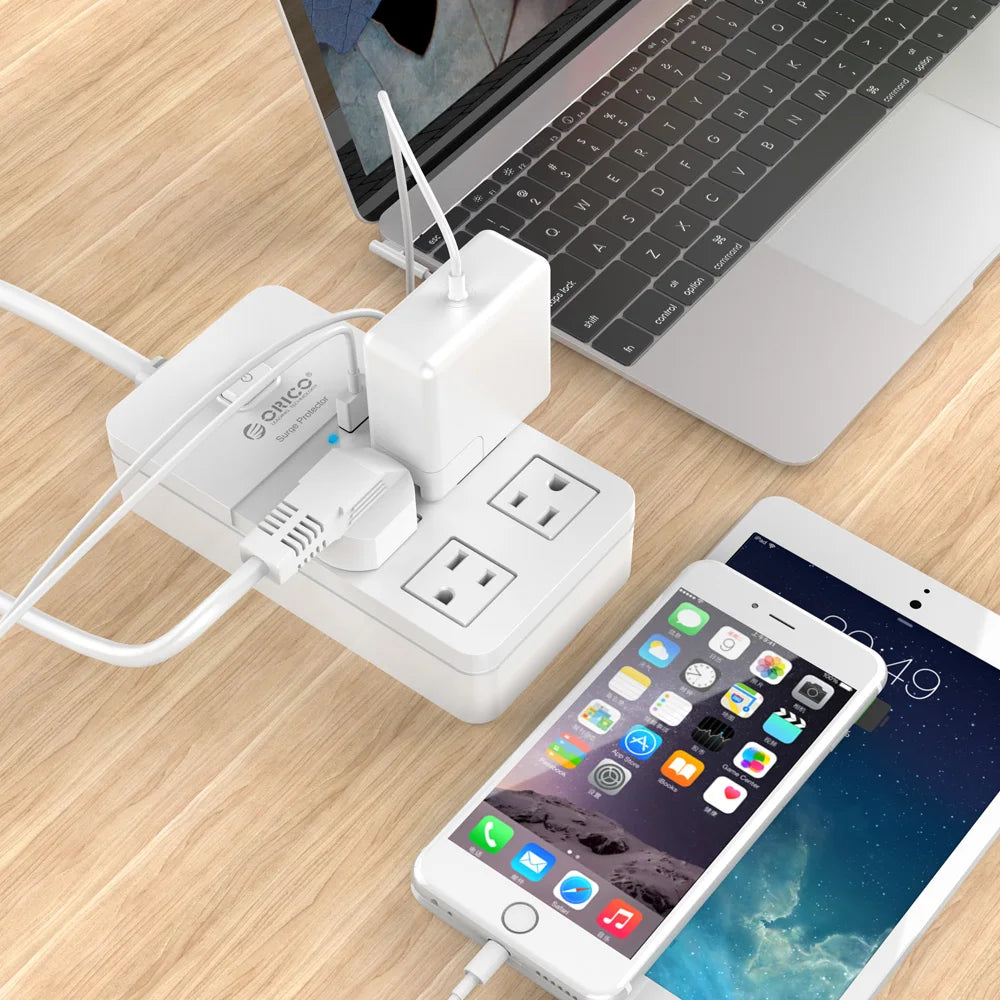Multiple electronic devices charging on a wooden surface with a laptop in the background.