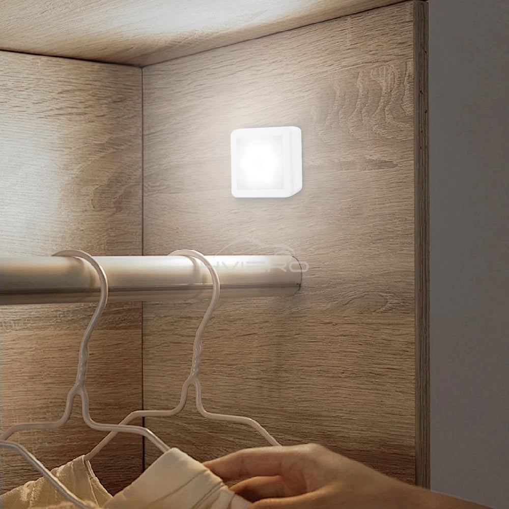 Square wall light fixture on a wooden wardrobe with hangers and a hand reaching in.